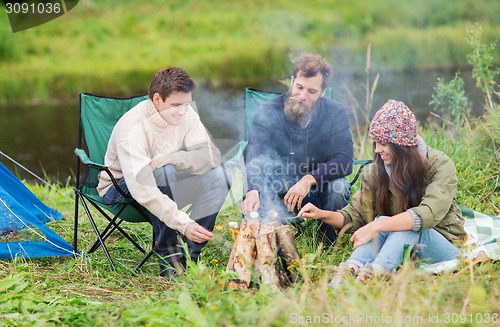 Image of smiling tourists cooking marshmallow in camping