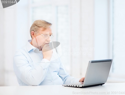 Image of old man in eyeglasses working with laptop at home