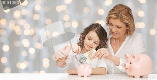 Image of mother and daughter putting money to piggy banks