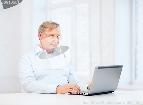 Image of old man in eyeglasses working with laptop at home