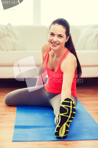 Image of smiling teenage girl streching on floor at home