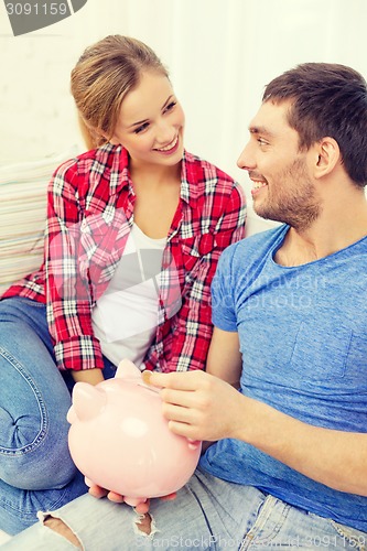 Image of smiling couple with piggybank sitting on sofa