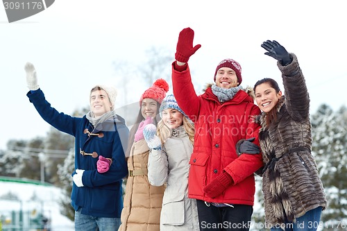 Image of happy friends waving hands on ice rink outdoors