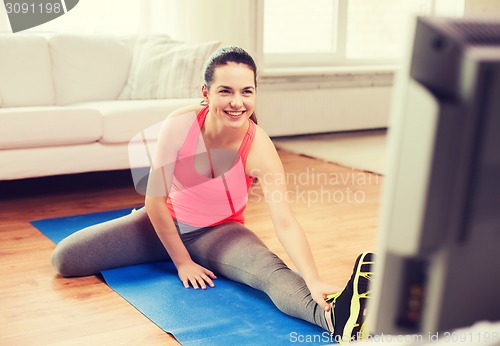 Image of smiling teenage girl streching on floor at home