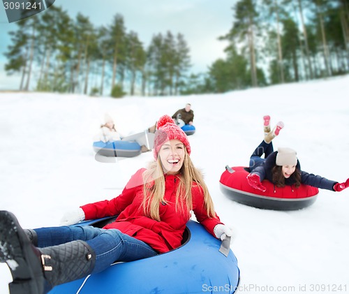 Image of group of happy friends sliding down on snow tubes