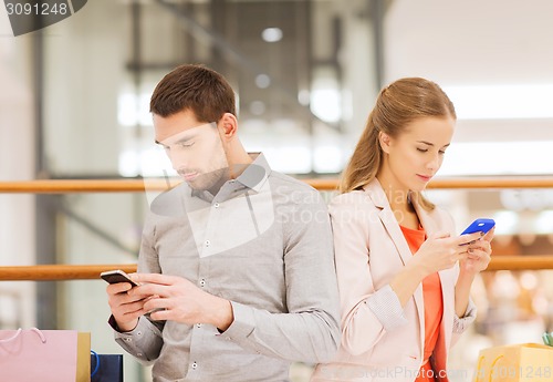 Image of couple with smartphones and shopping bags in mall