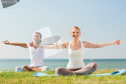 Image of smiling couple making yoga exercises outdoors