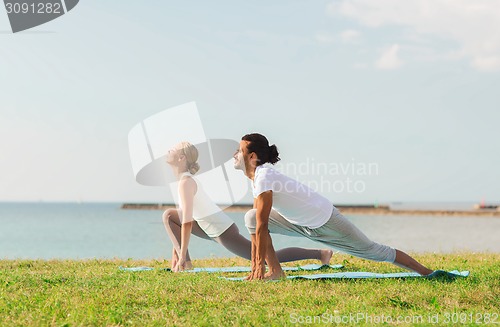 Image of smiling couple making yoga exercises outdoors