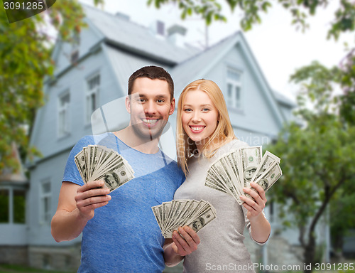 Image of smiling couple showing money over house background