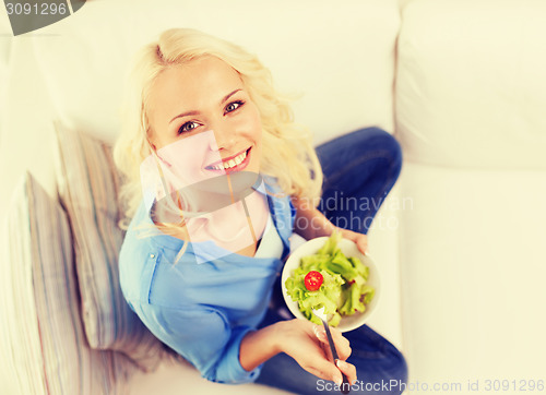 Image of smiling young woman with green salad at home