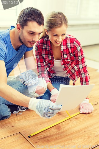 Image of smiling couple measuring wood flooring