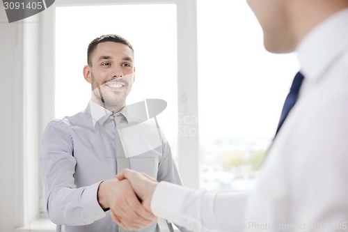 Image of two smiling businessmen shaking hands in office