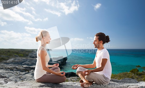 Image of happy couple meditating in lotus pose on beach