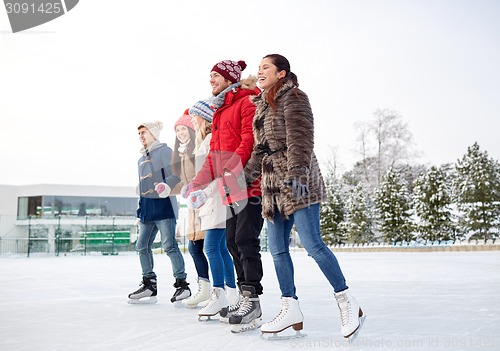 Image of happy friends ice skating on rink outdoors