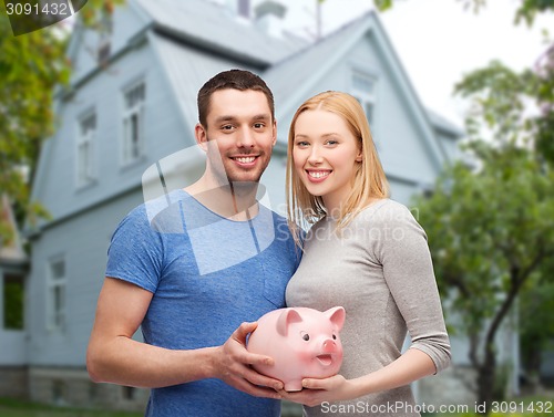 Image of smiling couple holding piggy bank over house