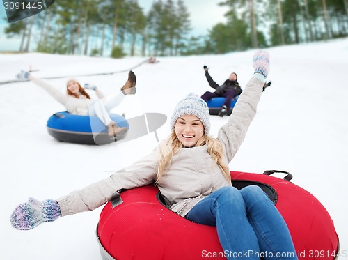 Image of group of happy friends sliding down on snow tubes