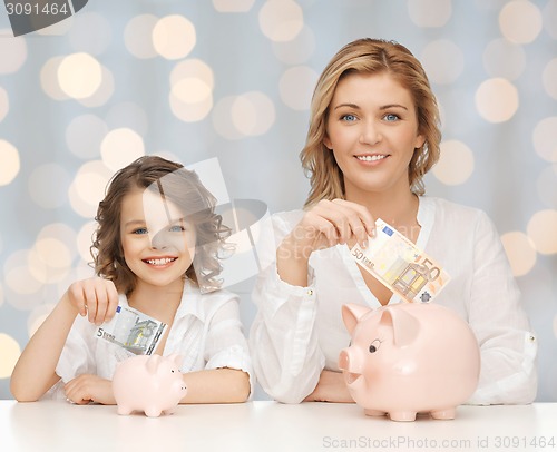 Image of mother and daughter putting money to piggy banks