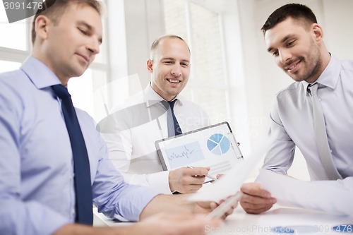 Image of smiling businessmen with papers in office