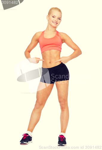 Image of smiling sporty woman pointing at her six pack