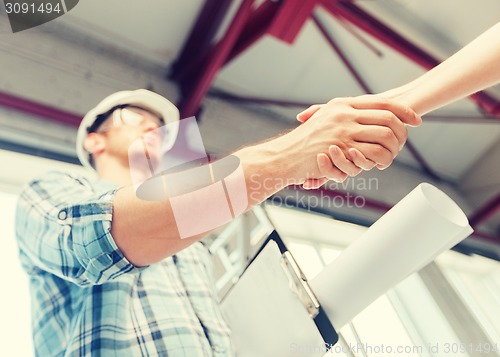 Image of builder with blueprint shaking partner hand