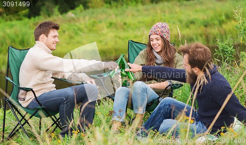 Image of group of smiling tourists drinking beer in camping
