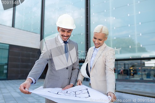 Image of smiling businessmen with blueprint and helmets