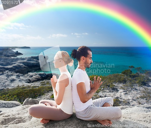 Image of happy couple meditating in lotus pose on beach