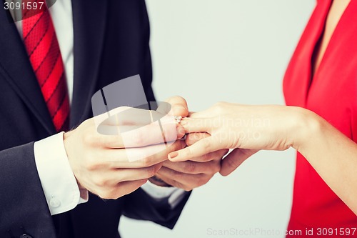 Image of man putting  wedding ring on woman hand