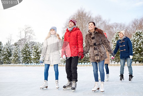 Image of happy friends ice skating on rink outdoors