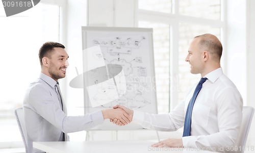 Image of two smiling businessmen shaking hands in office