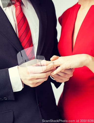 Image of man putting  wedding ring on woman hand