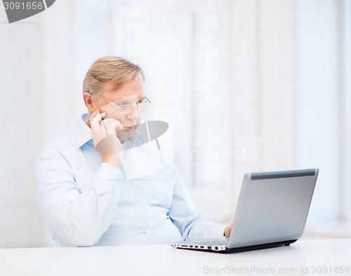 Image of old man in eyeglasses working with laptop at home