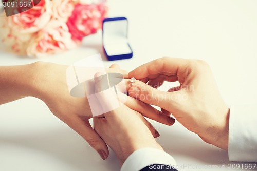 Image of man putting  wedding ring on woman hand