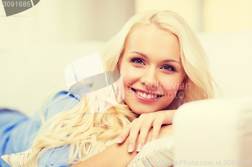 Image of smiling young woman lying on sofa at home