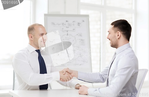 Image of two smiling businessmen shaking hands in office