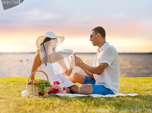 Image of smiling couple with small red gift box on picnic