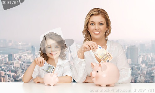 Image of mother and daughter putting money to piggy banks