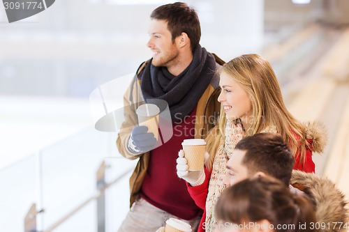 Image of happy friends with coffee cups on skating rink