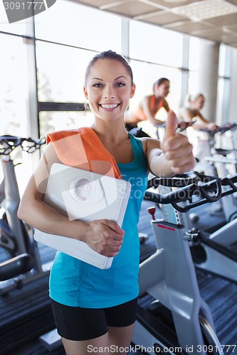 Image of smiling woman with scales and towel in gym