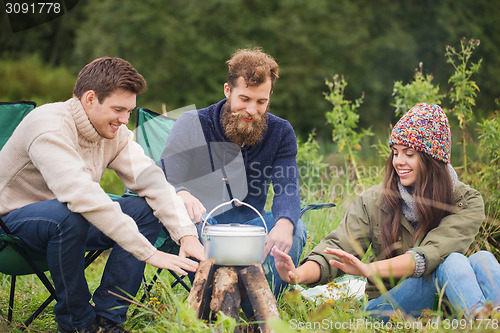 Image of group of smiling friends cooking food outdoors