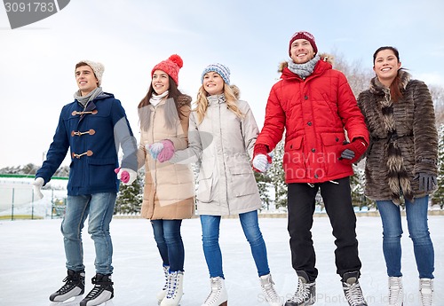 Image of happy friends ice skating on rink outdoors