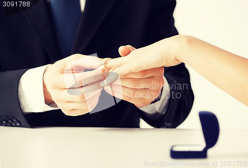 Image of man putting  wedding ring on woman hand