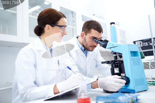 Image of scientists with clipboard and microscope in lab