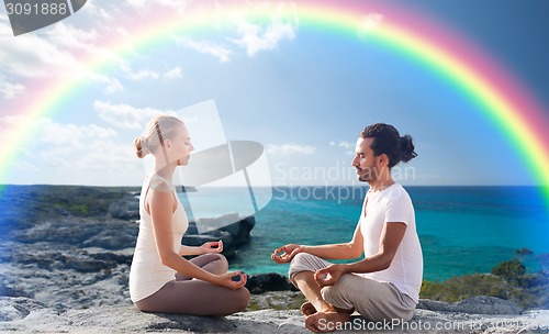 Image of happy couple meditating in lotus pose on beach