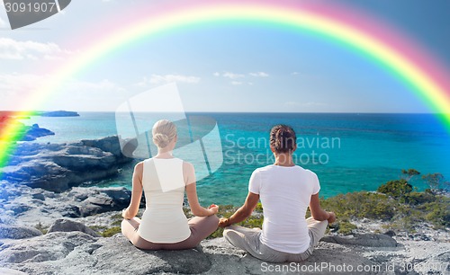 Image of happy couple meditating in lotus pose on beach