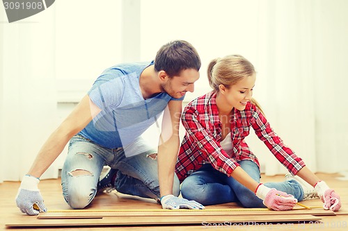 Image of smiling couple measuring wood flooring