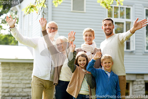 Image of happy family waving hands in front of house