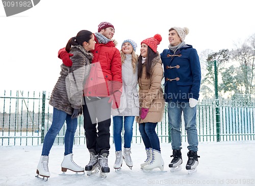 Image of happy friends ice skating on rink outdoors