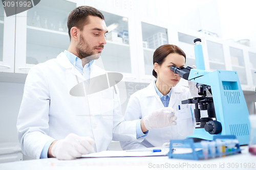 Image of scientists with clipboard and microscope in lab