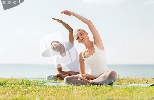 Image of smiling couple making yoga exercises outdoors